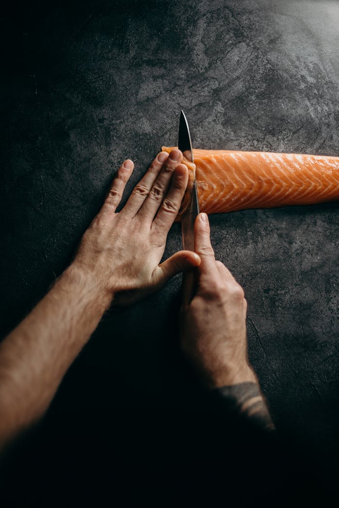 Mastering the First Impression: Your intriguing post title goes here Chef expertly slicing fresh salmon on dark surface, highlighting culinary skill and precision in food preparation.