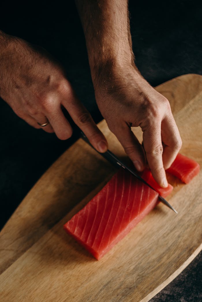 The Art of Drawing Readers In: Your attractive post title goes here A person skillfully slices fresh tuna sashimi on a wooden board, showcasing culinary expertise.