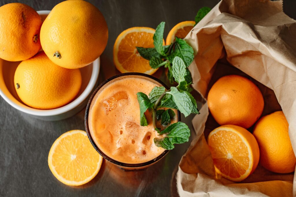 Top view of refreshing orange juice surrounded by fresh oranges and mint, perfect for a healthy boost.